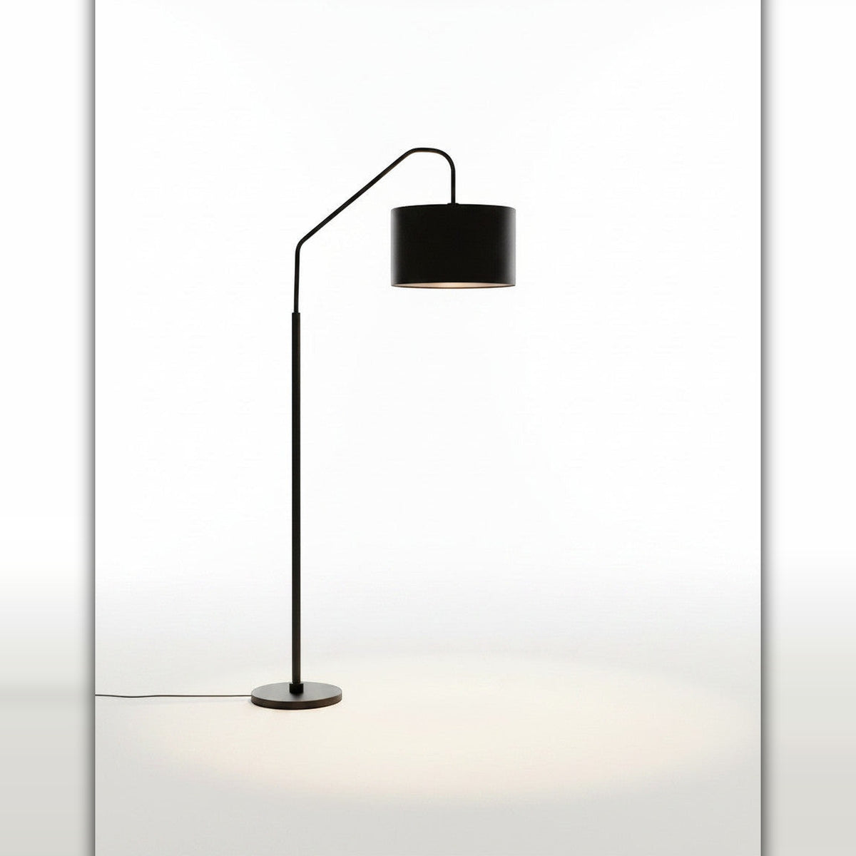 Lysverden sort buegulvlampe med sylindrisk stoffskjerm som gir mykt stemningslys i stuen.