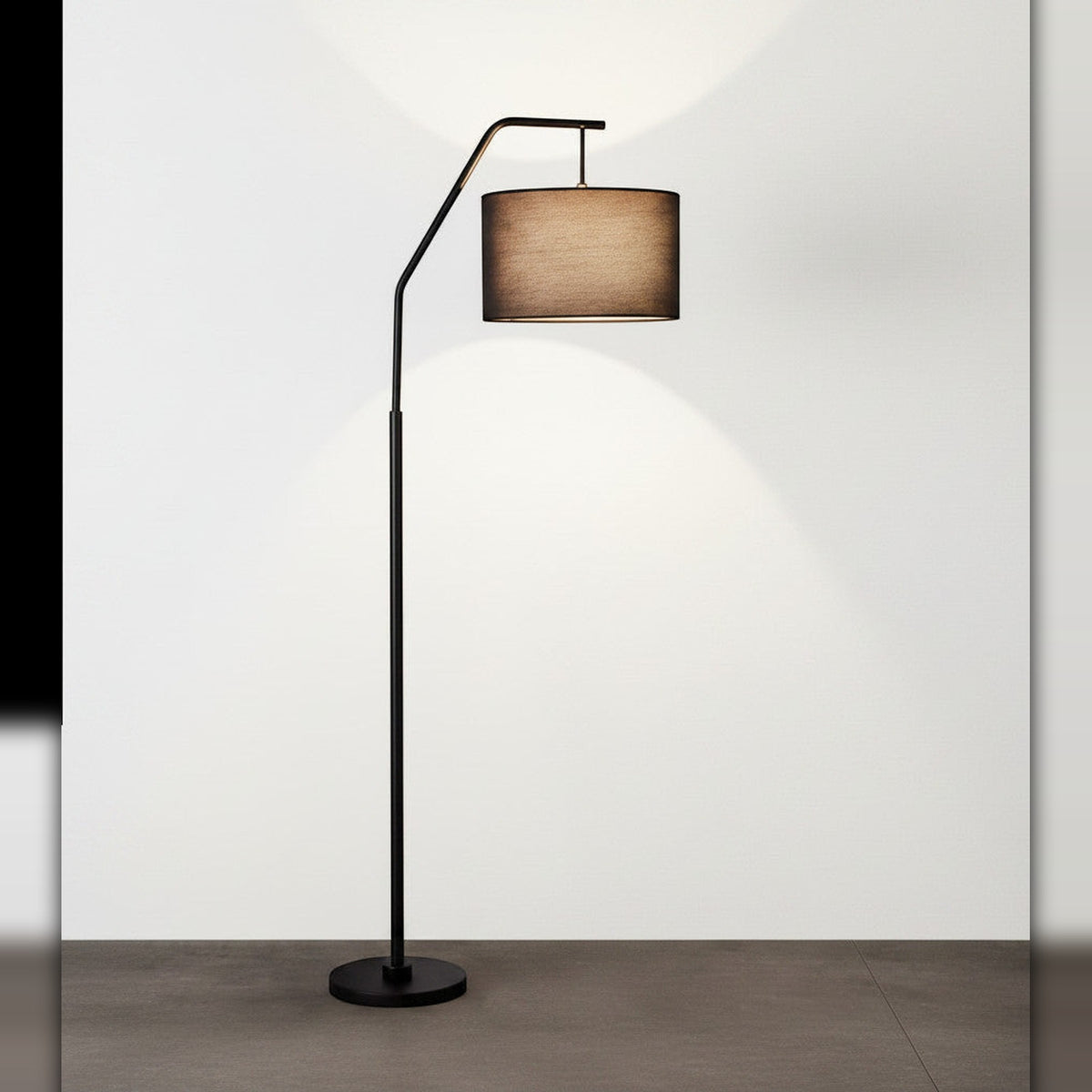 Lysverden sort buegulvlampe med sylindrisk stoffskjerm som gir varmt, diffust lys i stuen.