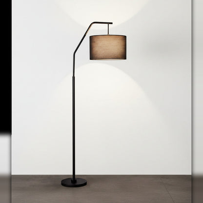 Lysverden sort buegulvlampe med sylindrisk stoffskjerm som gir varmt, diffust lys i stuen.