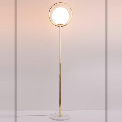 Lysverden gullfarget gulvlampe med sirkulær metallramme og hvit kule i opalglass på marmorfot.