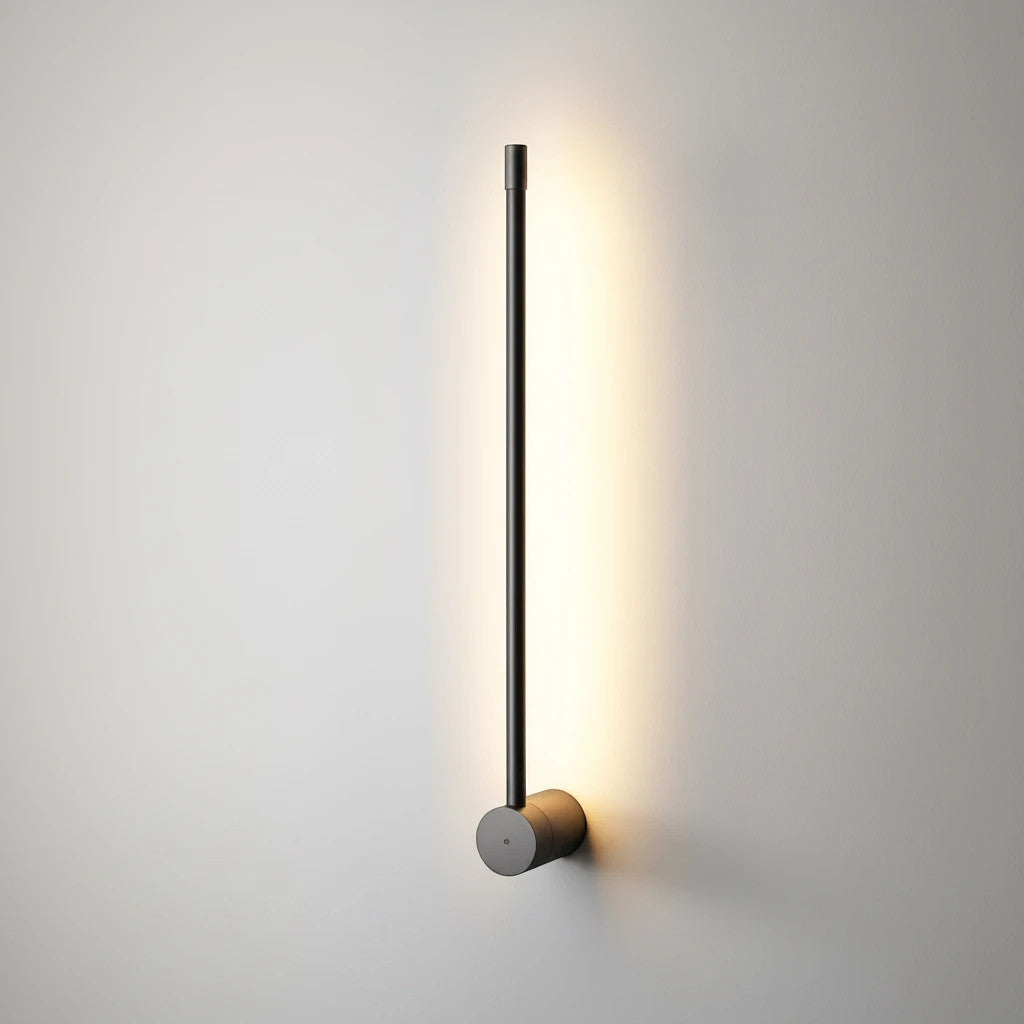 Lysverden LYS lineær sort LED-vegglampe med minimalistisk vertikal design som gir varmt lys mot en lys vegg