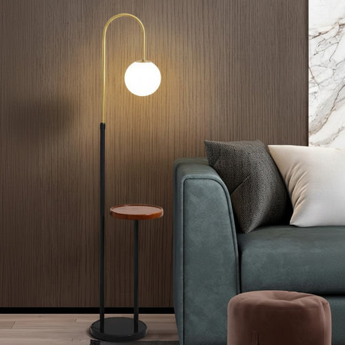 Lysverden modern arched floor lamp with gold arm, black base, and integrated side table holding an opal glass globe.