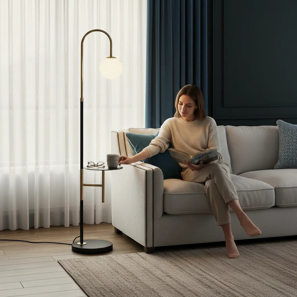Lysverden modern gold and black arched floor lamp with opal glass globe and integrated side table in a living room.
