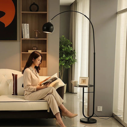 Lysverden black arched floor lamp with a stone base and glass shade, positioned next to a sofa with a woman reading.