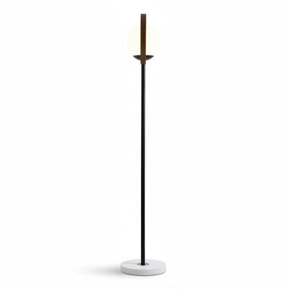 Lysverden moderne gulvlampe med sort metallstamme, sirkelramme og lysende kule i opalglass på hvit fot.