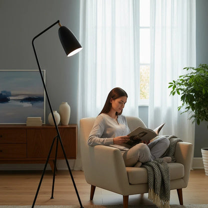 Lysverden black tripod floor lamp with adjustable cone shade illuminating a woman reading in a cozy living room