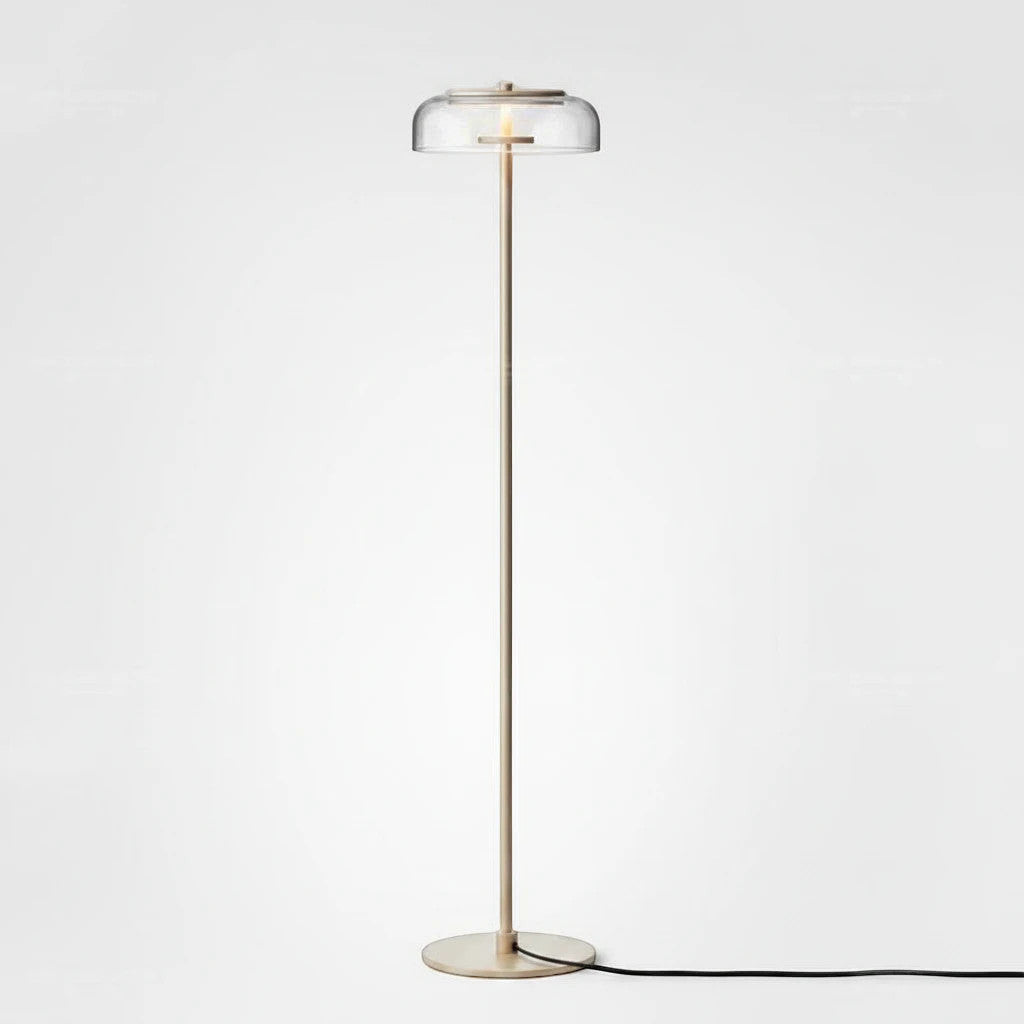 Lysverden floor lamp with a slim brass stem and a clear glass disc shade providing warm LED light in a modern style.