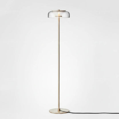 Lysverden floor lamp with a slim brass stem and a clear glass disc shade providing warm LED light in a modern style.
