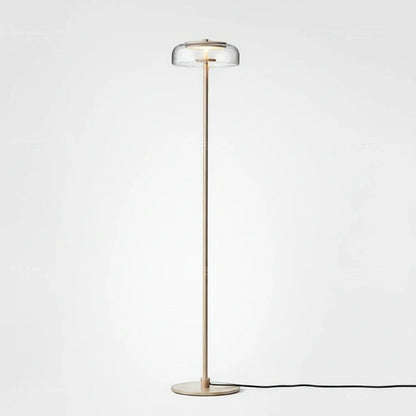 Lysverden elegant floor lamp with a slim brass stem and a clear glass disc shade emitting warm LED light.