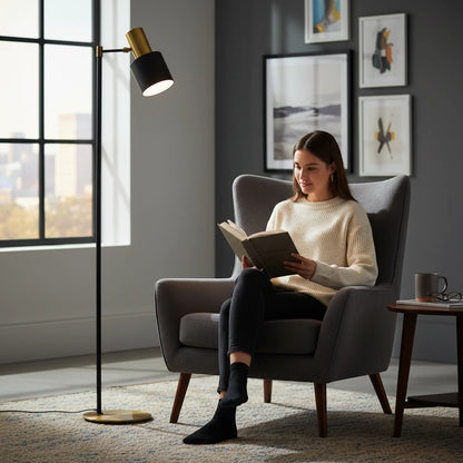 Lysverden classic floor reading lamp with black shade and brass base next to a woman reading in a grey armchair