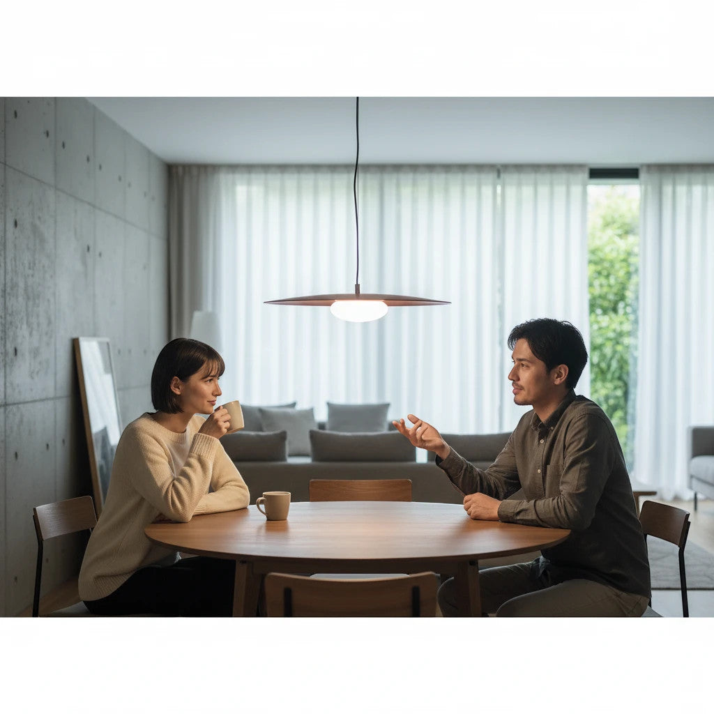 Lysverden copper disc pendant lamp with opal glass globe hanging over a wooden dining table with a couple talking.