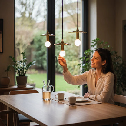 Lysverden disc pendant lights with brass details hanging over a wooden dining table as a woman adjusts a bulb