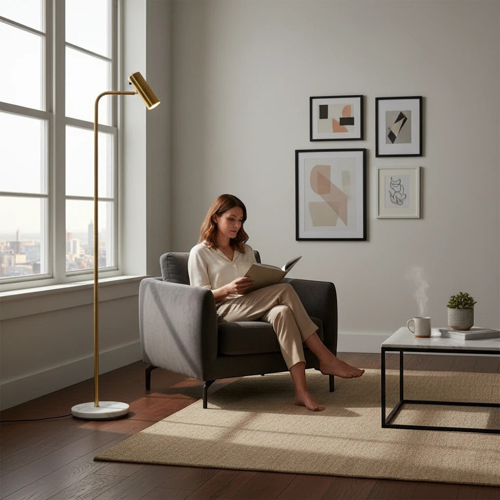 Lysverden minimalist gold floor lamp with marble base providing focused reading light for a woman in a grey armchair.