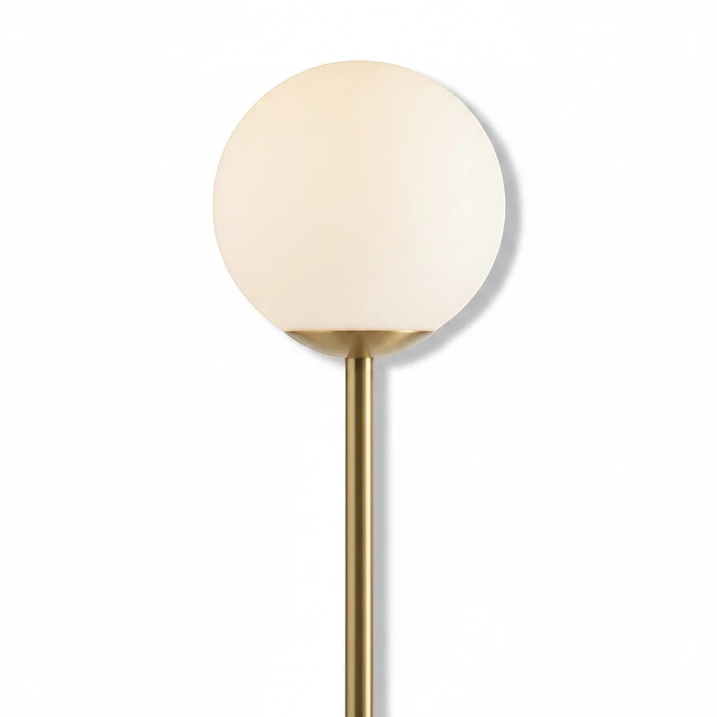 Lysverden minimalistisk gulvlampe med matt kule i opalglass på slank gullfarget metallstamme for varmt stemningslys.