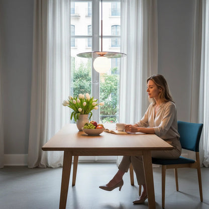 Lysverden Gulldisk pendant lamp with a white opal glass globe and gold disc, hanging over a wooden dining table.