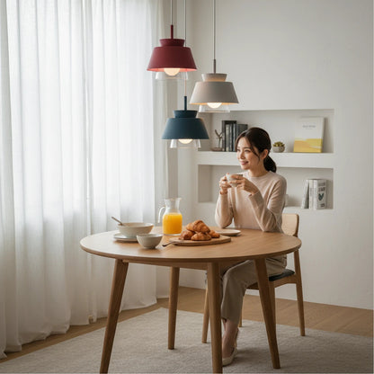 Lysverden Macaron pendant lights in red, blue, and grey hanging over a wooden dining table with a woman sitting.