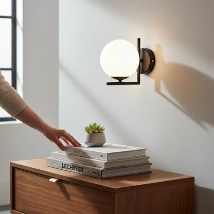 Lysverden modern wall lamp with a round opal glass globe and black geometric frame mounted above a wooden bedside table.