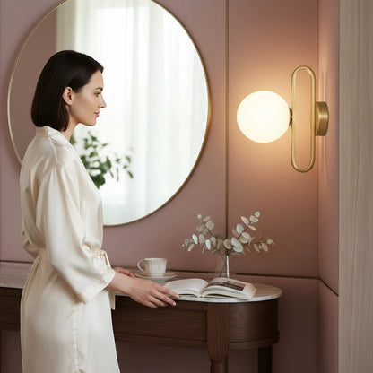 Lysverden wall lamp with a spherical glass shade and gold frame mounted in a modern bedroom with a woman reading