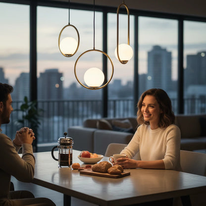 Lysverden opal glass pendant lights with gold rings hanging over a dining table in a modern apartment at sunset.