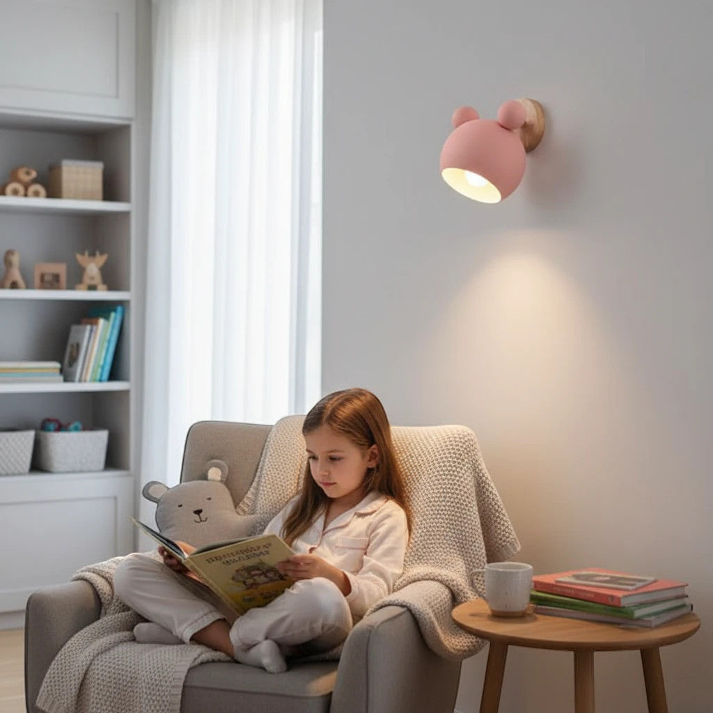 Lysverden pink bear-shaped LED wall lamp with wooden detail, mounted in a cozy child's room above a reading chair.