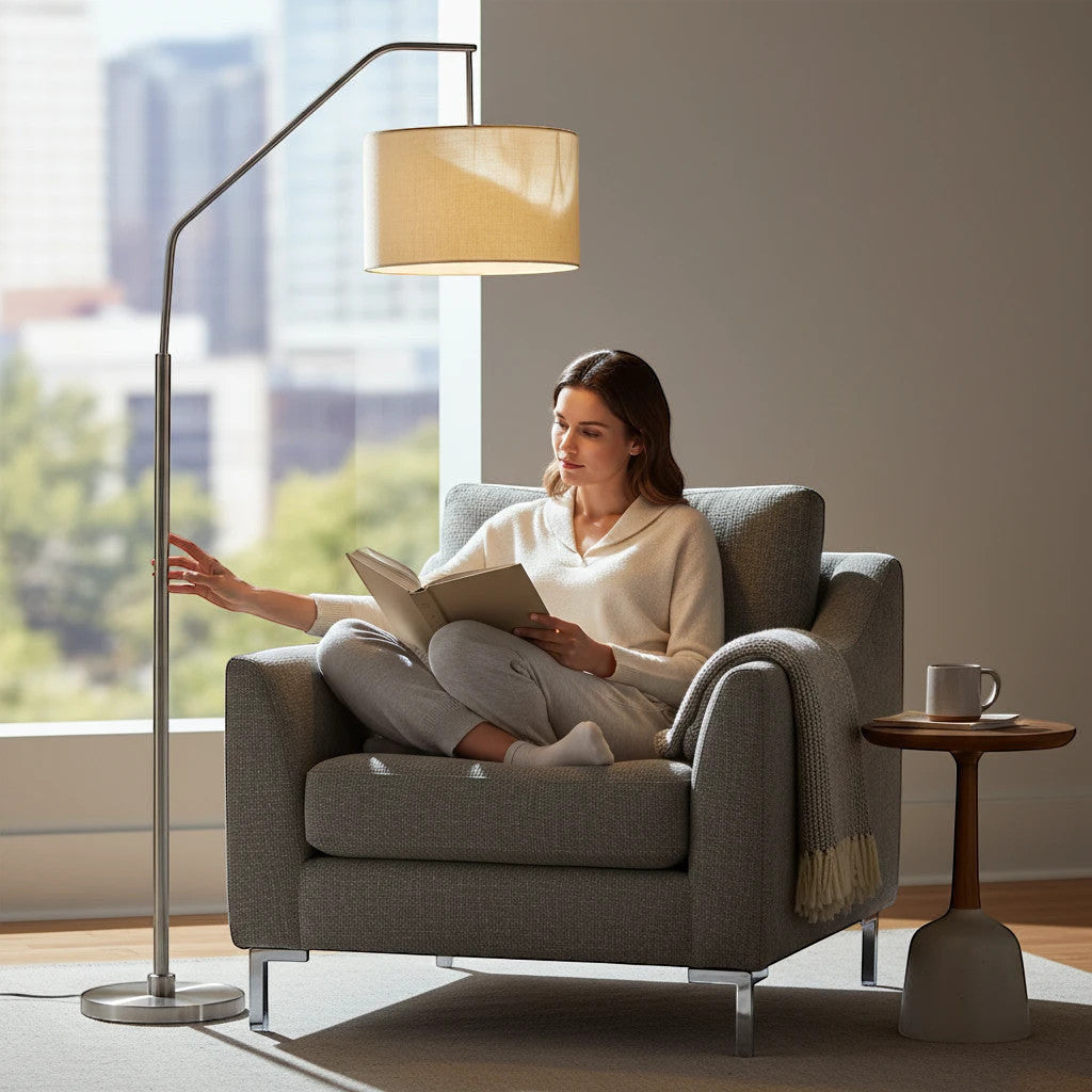 Lysverden silver arched floor lamp with fabric shade providing warm reading light over a woman in a grey armchair.