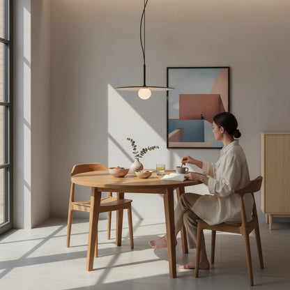 Lysverden minimalist pendant lamp with a flat black disc and opal glass globe hanging over a wooden dining table.