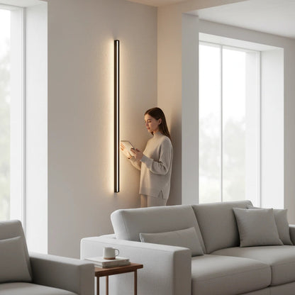 Lysverden minimalist black linear LED wall lamp mounted vertically in a modern living room with a woman reading.