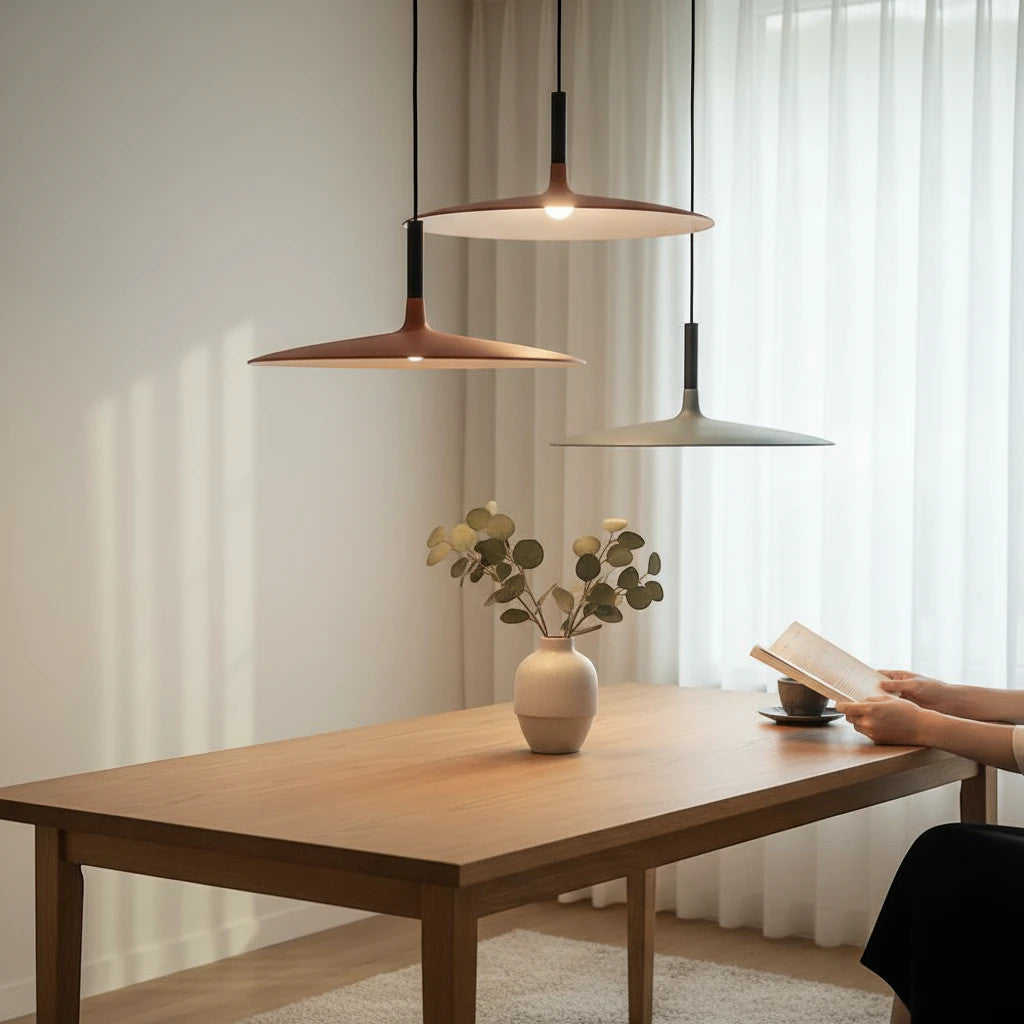 Lysverden modern tilted disk pendant lights in coffee and grey hanging over a wooden dining table with a person reading