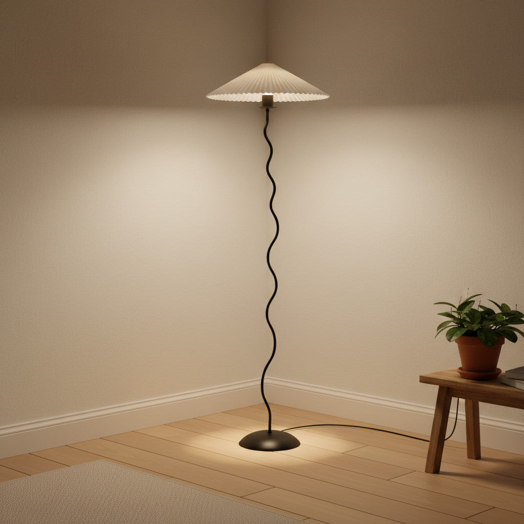 Lysverden sculptural floor lamp with a black wavy metal stem and a white pleated disc shade in a cozy room corner.