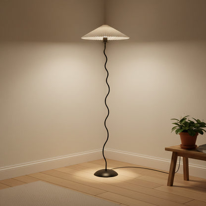 Lysverden sculptural floor lamp with a black wavy metal stem and a white pleated disc shade in a cozy room corner.