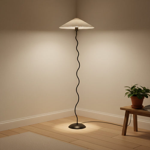 Lysverden sculptural floor lamp with a black wavy metal stem and a white pleated disc shade in a cozy room corner.
