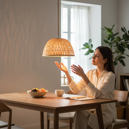 Lysverden woven bamboo pendant lamp casting warm light over a woman sitting at a wooden dining table in a Japandi room