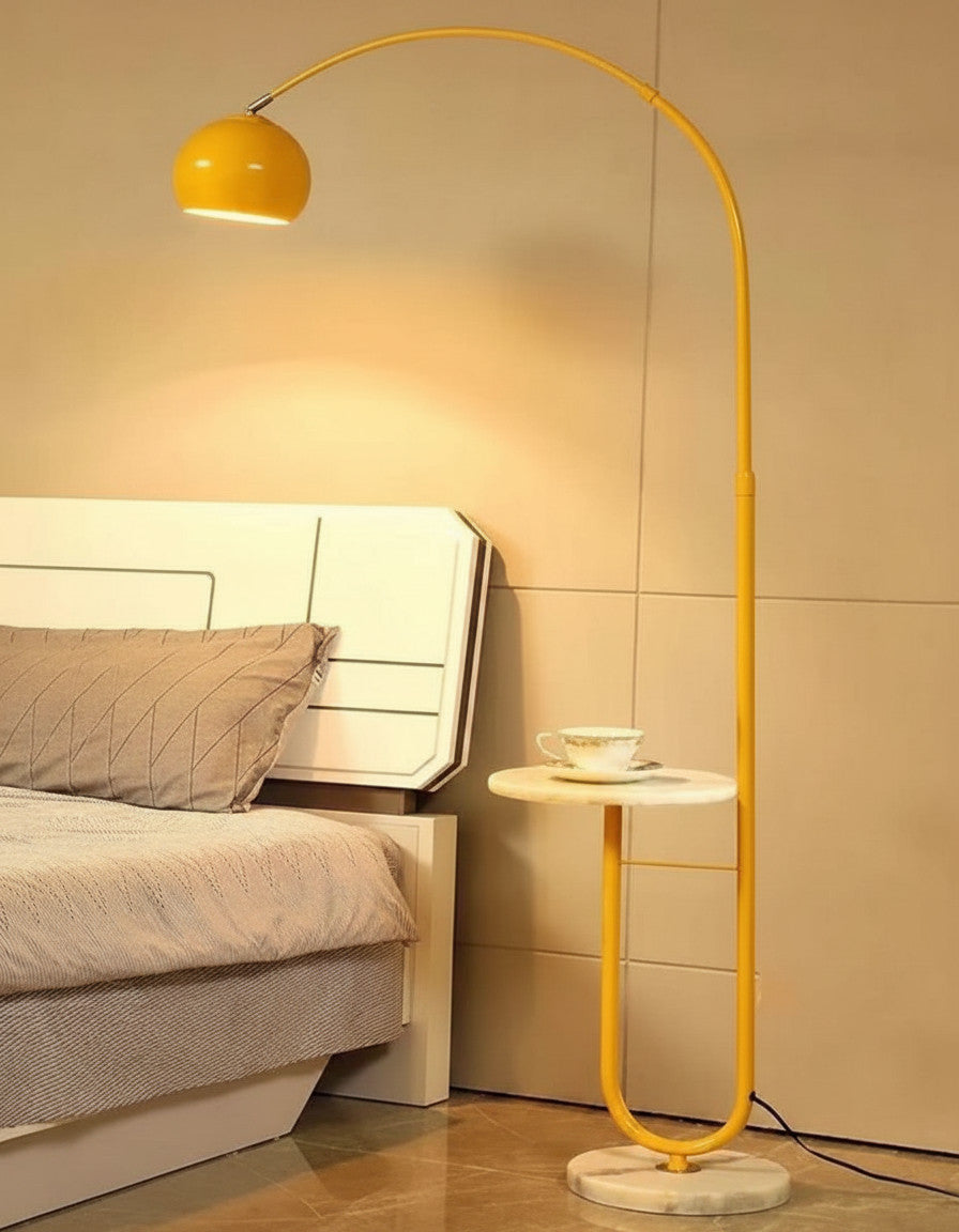 Lysverden yellow arched floor lamp with a stone base and integrated side table next to a bed in a modern bedroom.