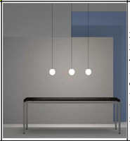 Slank sort pendellampe med lysende hvit glasskule over spisebord