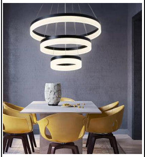 Sort LED-lysekrone med tre konsentriske lysende ringer over spisebord
